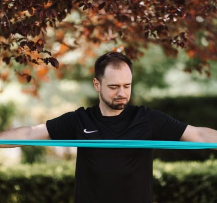 Man using resistance band for exercise in a sunny outdoor setting.