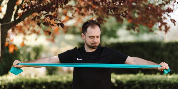 Man using resistance band for exercise in a sunny outdoor setting.