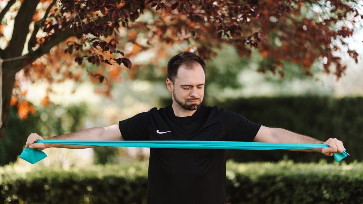 Man using resistance band for exercise in a sunny outdoor setting.